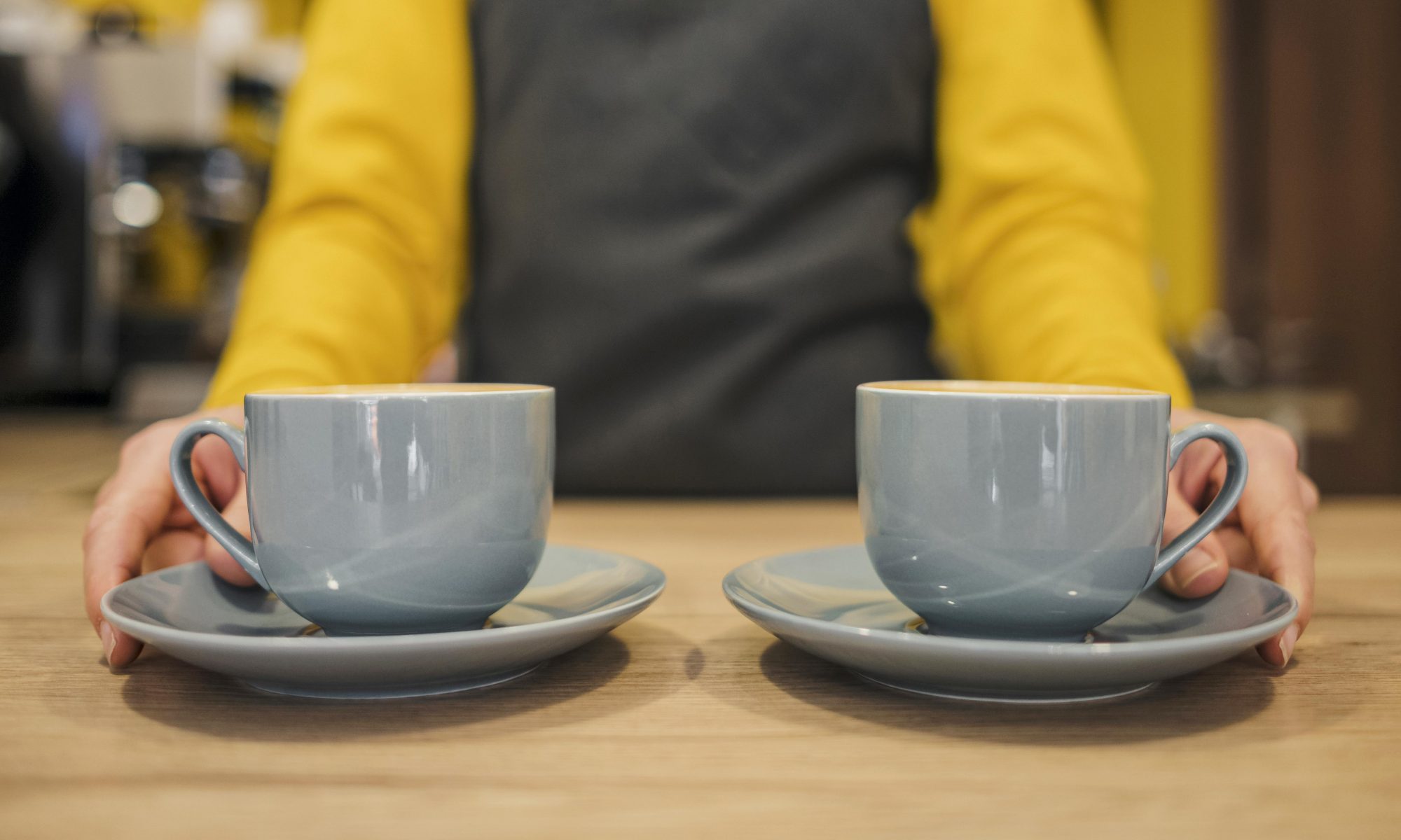 Två kaffekoppar på ett bord framför en diffus person